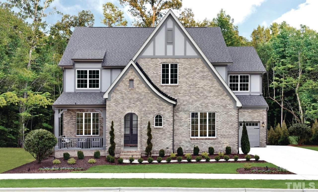 A gray brick, stone textured home with a covered porch, arched entryway, and manicured landscaping
